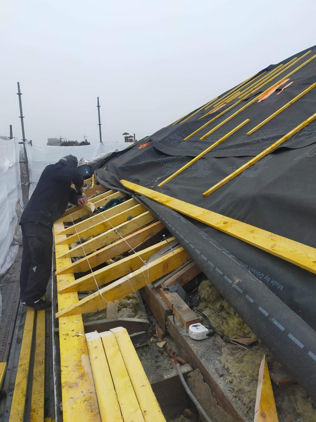Toit d'un bâtiment avec des bardeaux gris foncé, un mur beige et un ciel bleu.