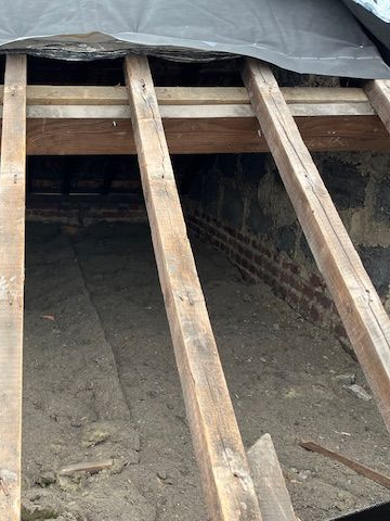 Vue intérieure d'un grenier inachevé avec des chevrons et des blocs de bois empilés au premier plan.