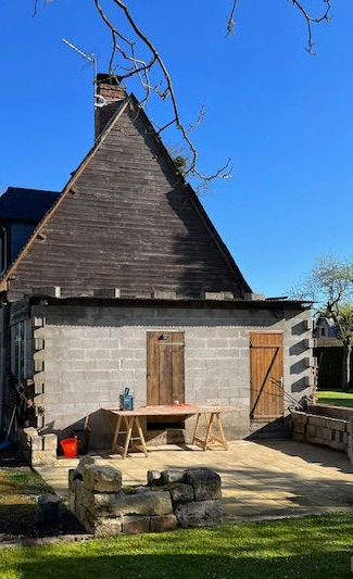 Camion garé près d'un bâtiment en pierre grise avec des volets en bois et un toit patiné par les intempéries par une journée ensoleillée.