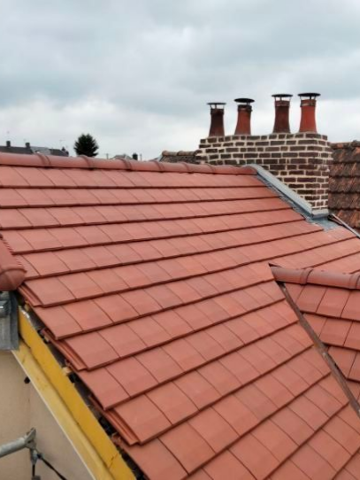 Toit de tuiles rouges avec cheminées en briques contre un ciel nuageux.