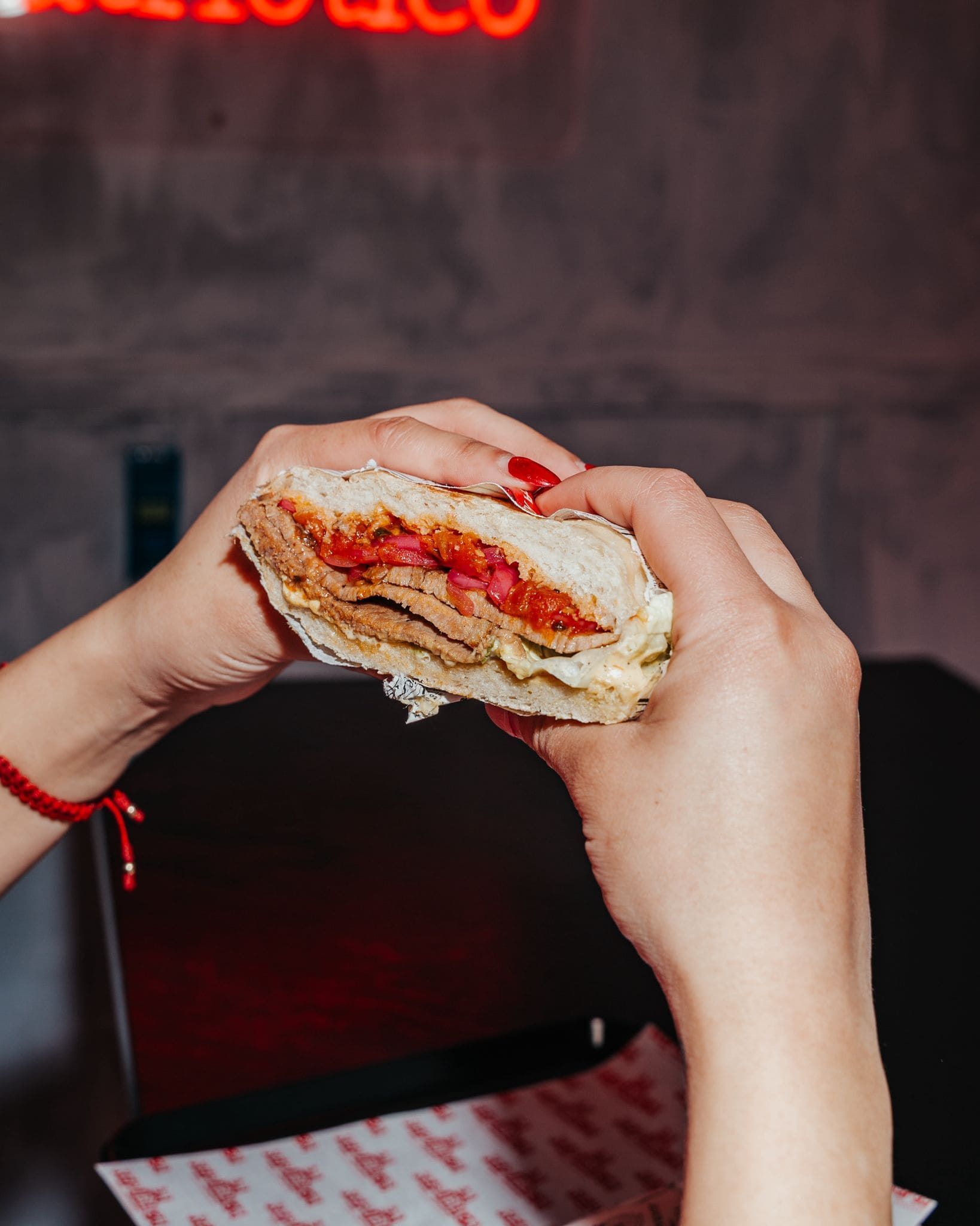 Manos sosteniendo y separando un sándwich, dejando al descubierto el relleno; pulsera roja visible.