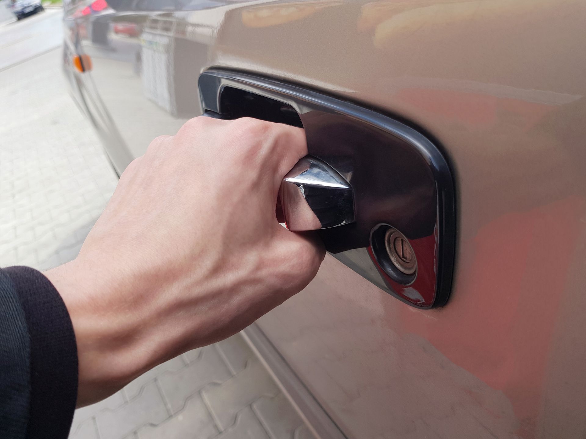 Une main tirant la poignée de la portière d'une voiture beige.