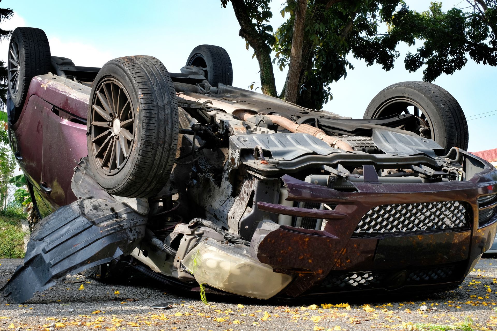 Une voiture bordeaux accidentée, renversée sur le toit près d'un arbre, l'avant endommagé et des débris éparpillés à proximité.
