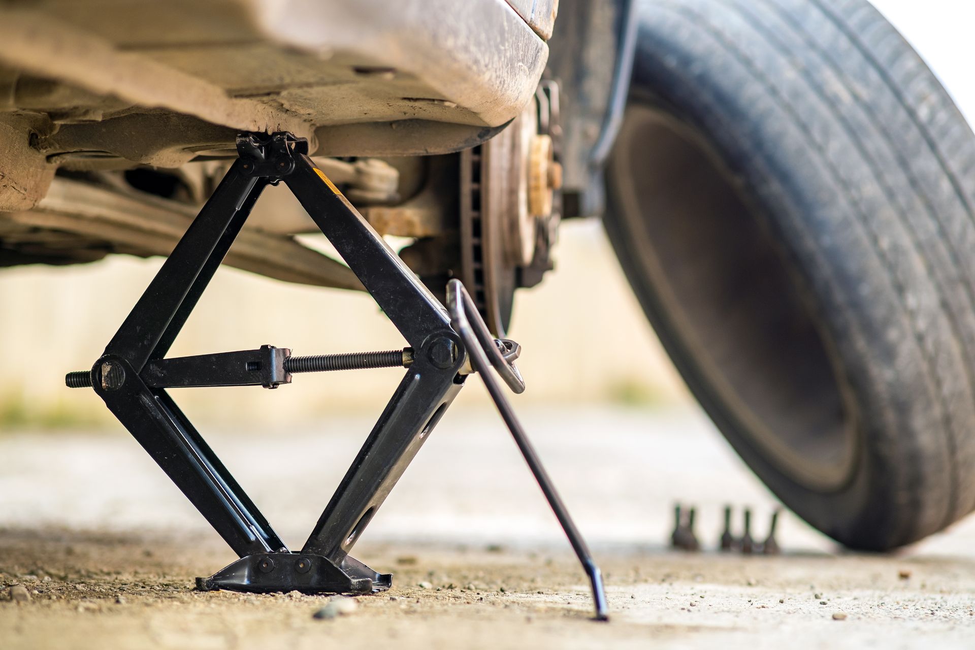 Un cric soulève une voiture dont une roue a été retirée, en bord de route.