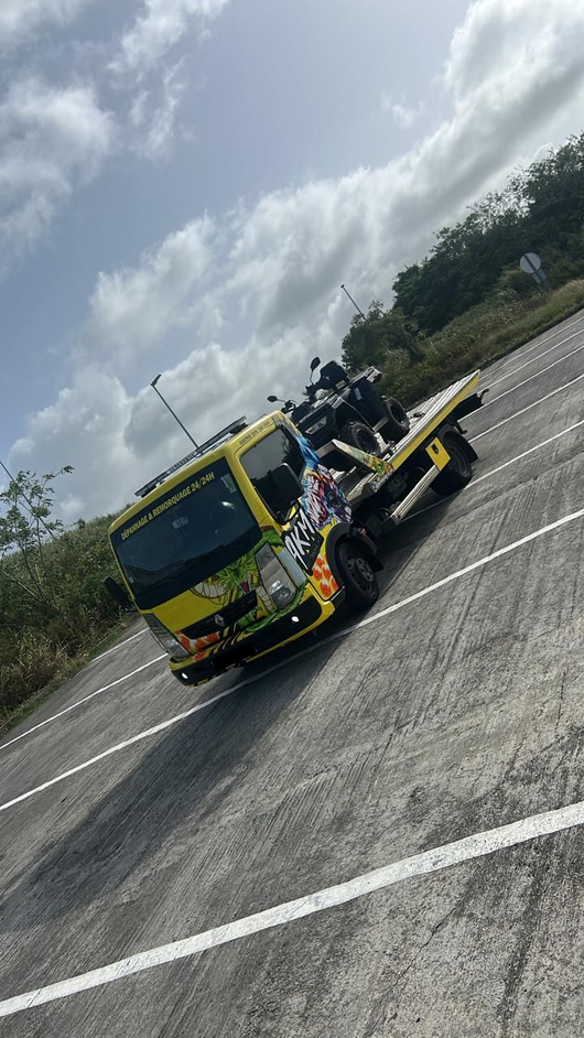 Camion de dépannage jaune incliné sur un parking sous un ciel nuageux
