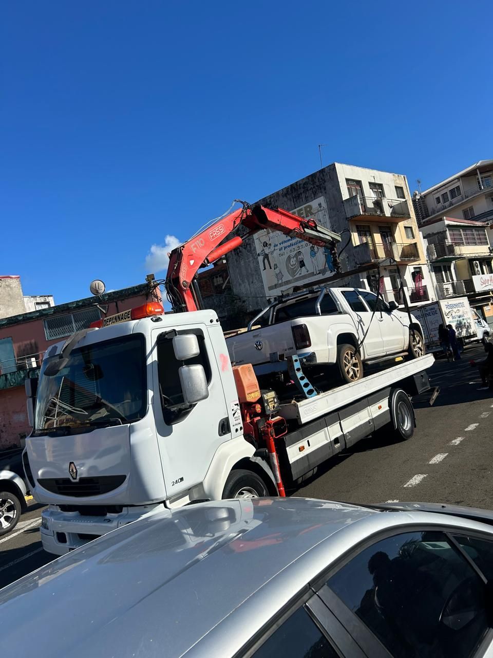 Une dépanneuse charge une camionnette blanche dans une rue de la ville sous un ciel bleu.