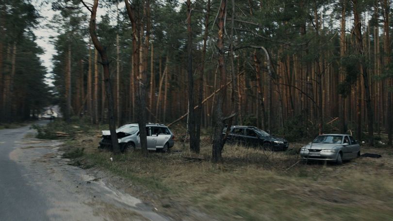 Des voitures endommagées garées parmi les arbres au bord d'un chemin de terre dans une clairière.