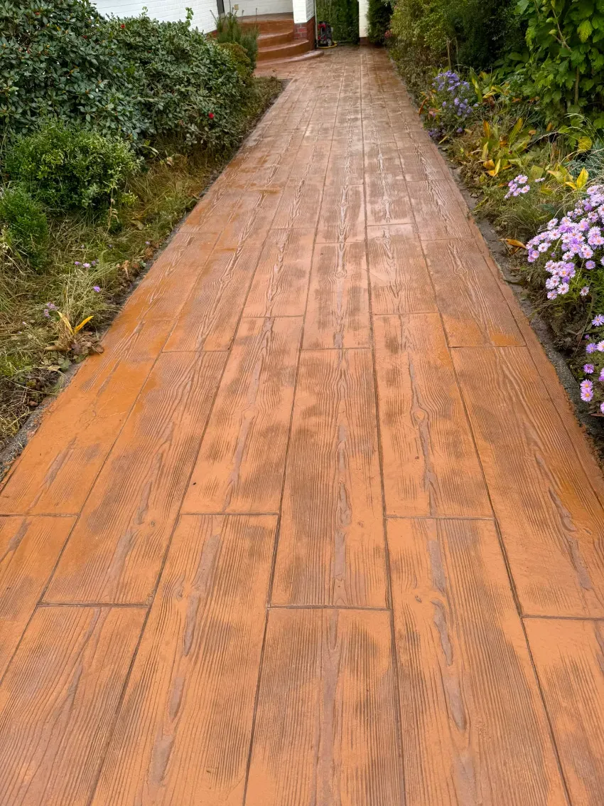 Sendero de madera en el jardín bordeado de arbustos verdes y flores moradas.