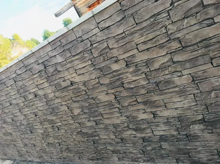 Muro de piedra con mampostería gris apilada, visto desde un ángulo en el exterior.