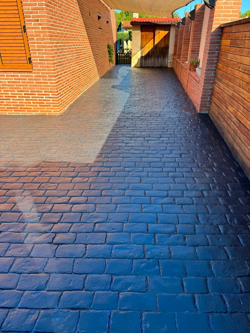 Pasarela de ladrillo entre edificios, con adoquines iluminados y sombreados que conducen a un pasaje cubierto.
