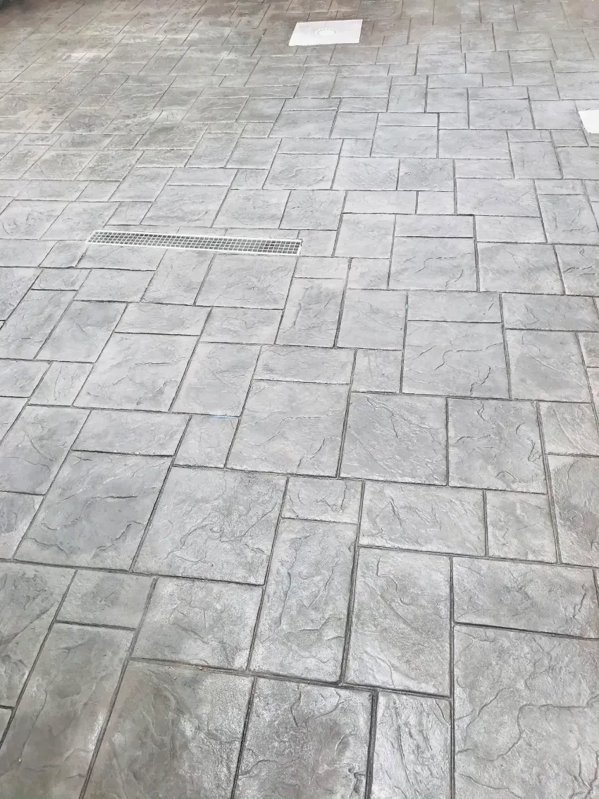 Pavimento de losas de piedra gris con una tapa de mantenimiento rectangular cerca de la parte superior.