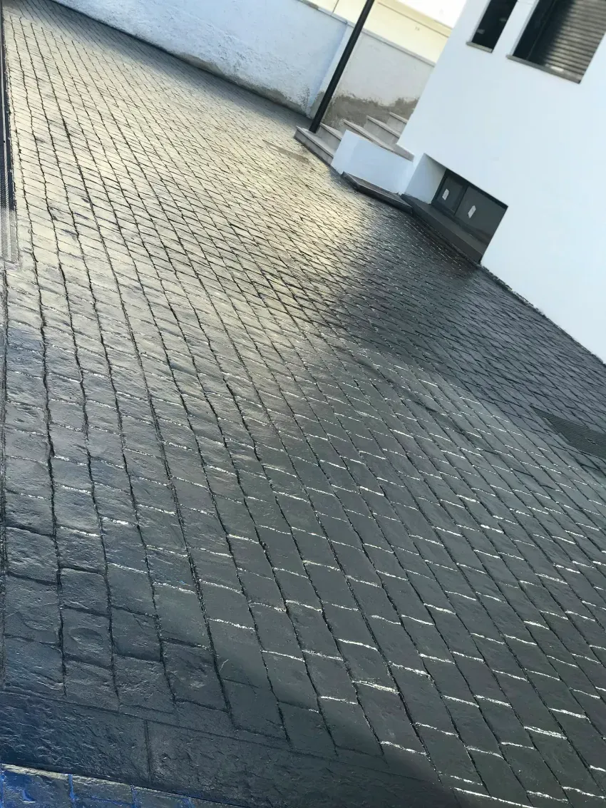 Vista inclinada de un sendero empedrado junto a un edificio blanco bajo la luz del sol.