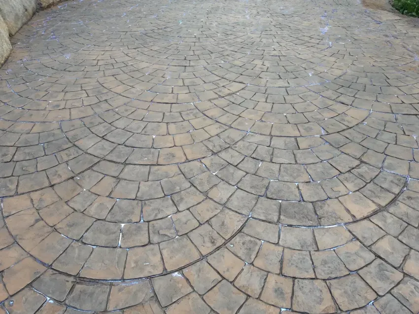 Patio curvo de adoquines de piedra en tonos grises y tostados.
