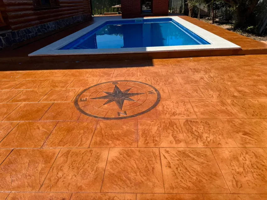 Patio de hormigón estampado de color naranja con diseño de brújula junto a una piscina azul.