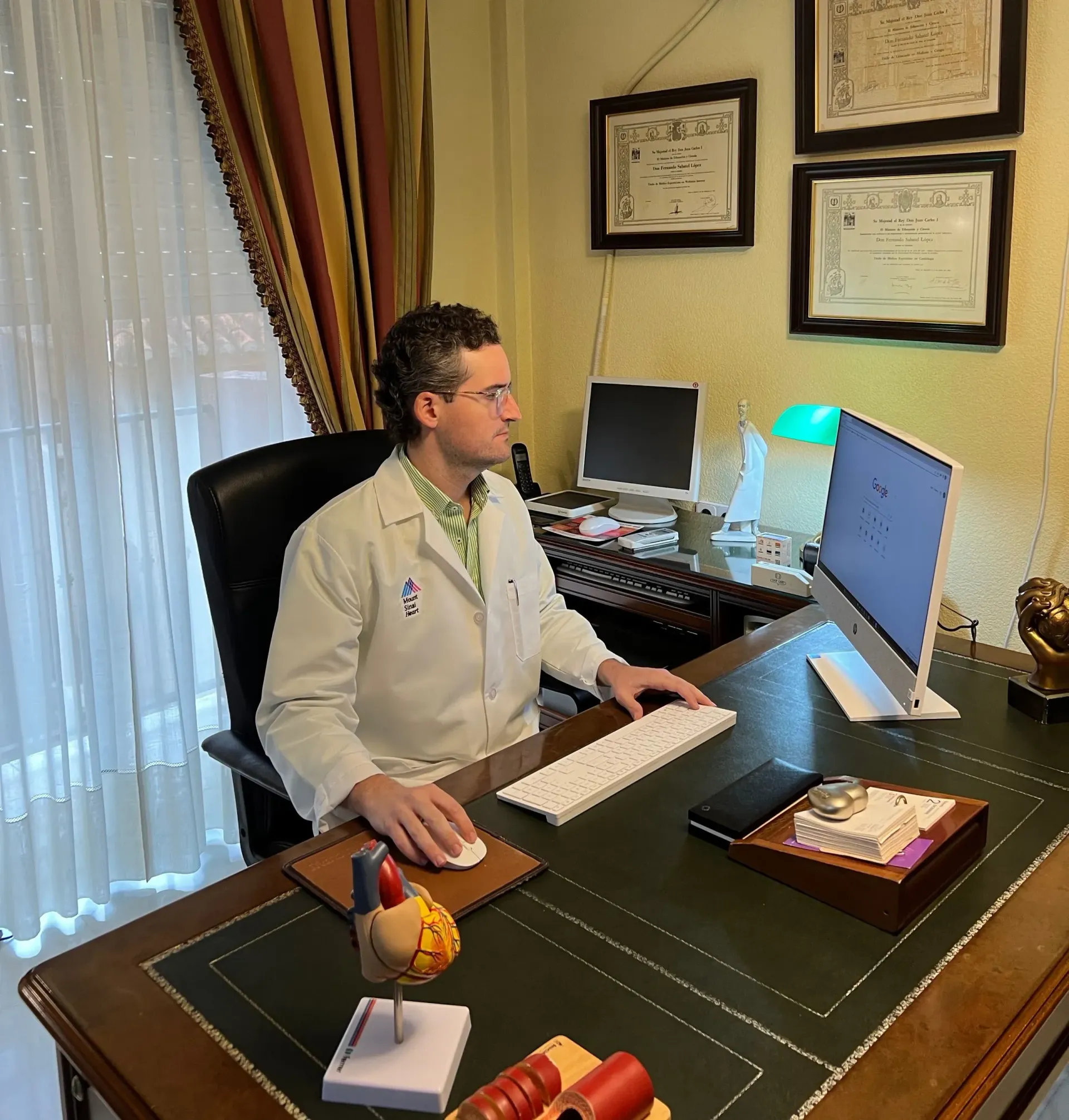 Un hombre con bata de laboratorio está sentado en un escritorio con una computadora.