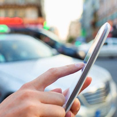 Primer plano de la mano de una persona usando un teléfono inteligente en una calle de la ciudad, con un coche borroso al fondo.