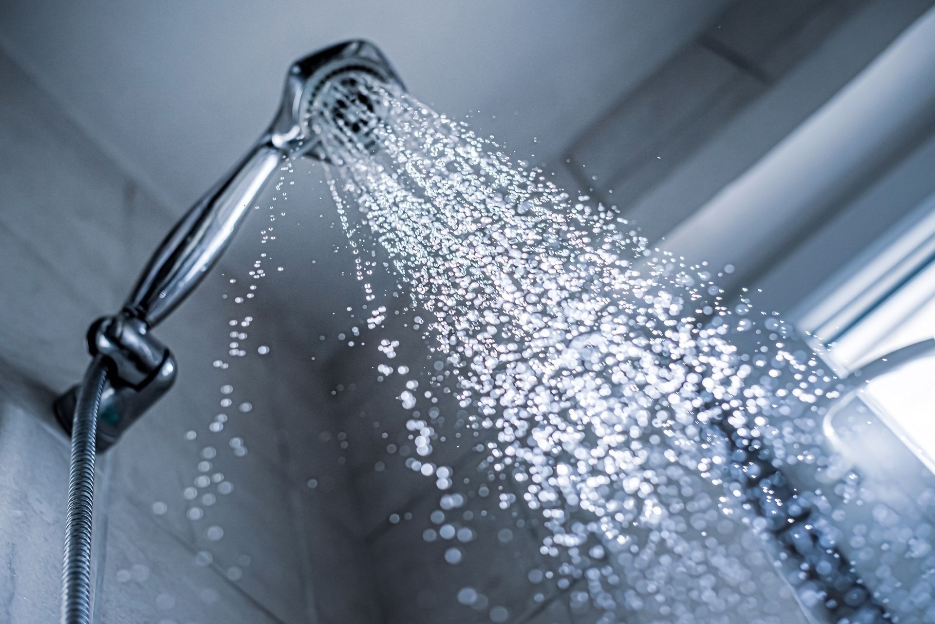 Pommeau de douche chromé projetant de l’eau contre un mur de salle de bains carrelé