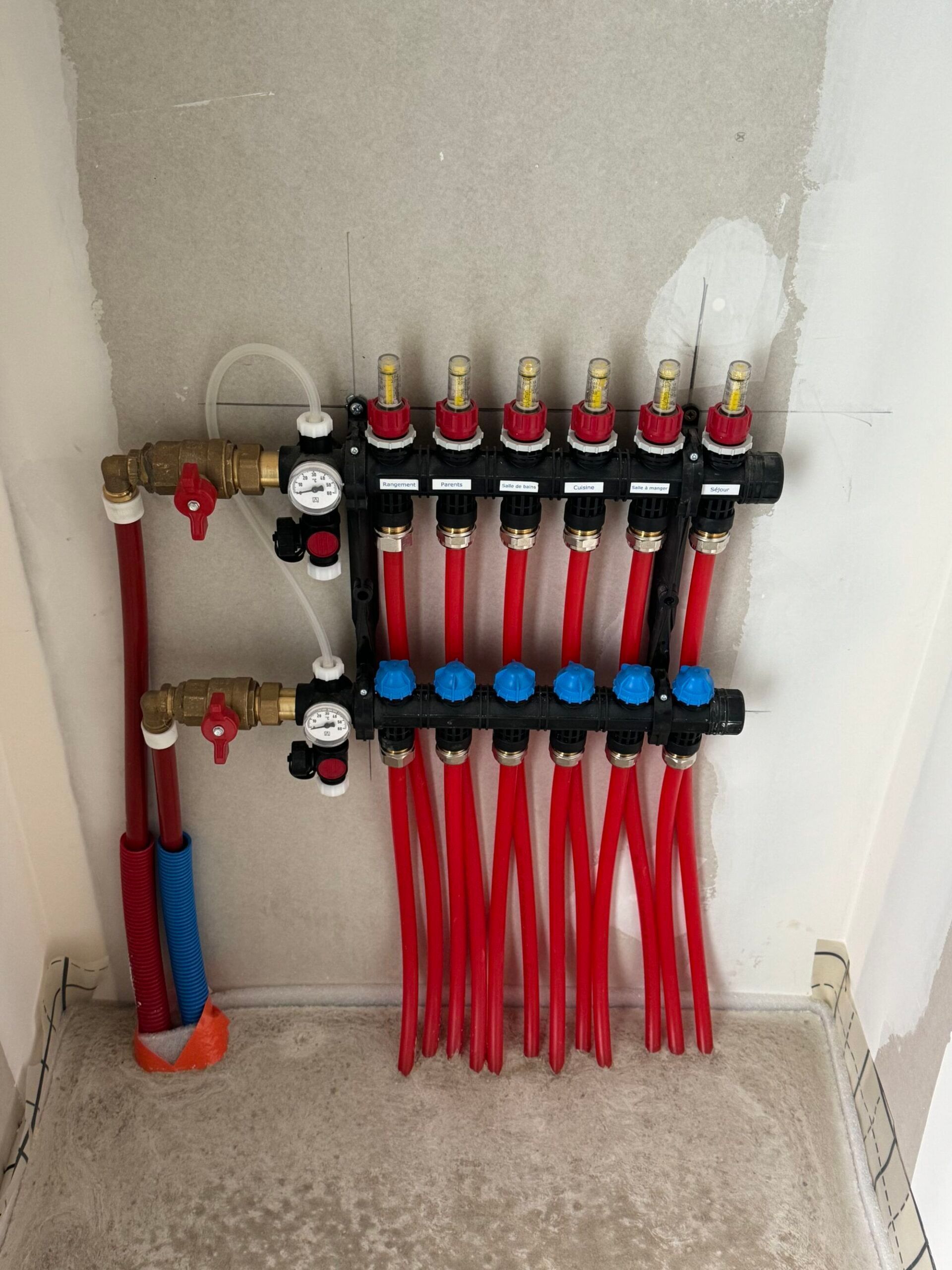 Collecteur de plomberie, avec des tuyaux et des vannes rouges et bleues, installé dans une niche murale