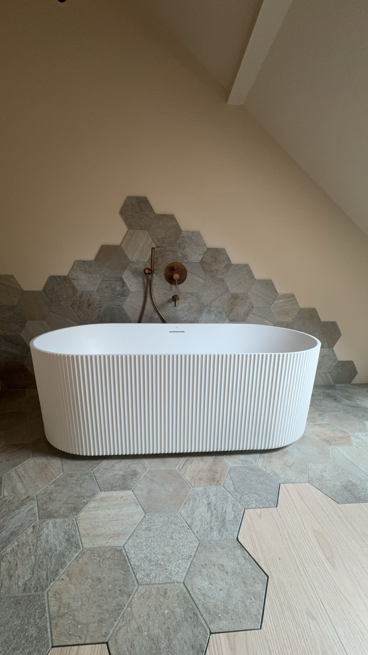 Baignoire blanche autoportante devant un mur d’accent en carreaux hexagonaux dans une salle de bains carrelée