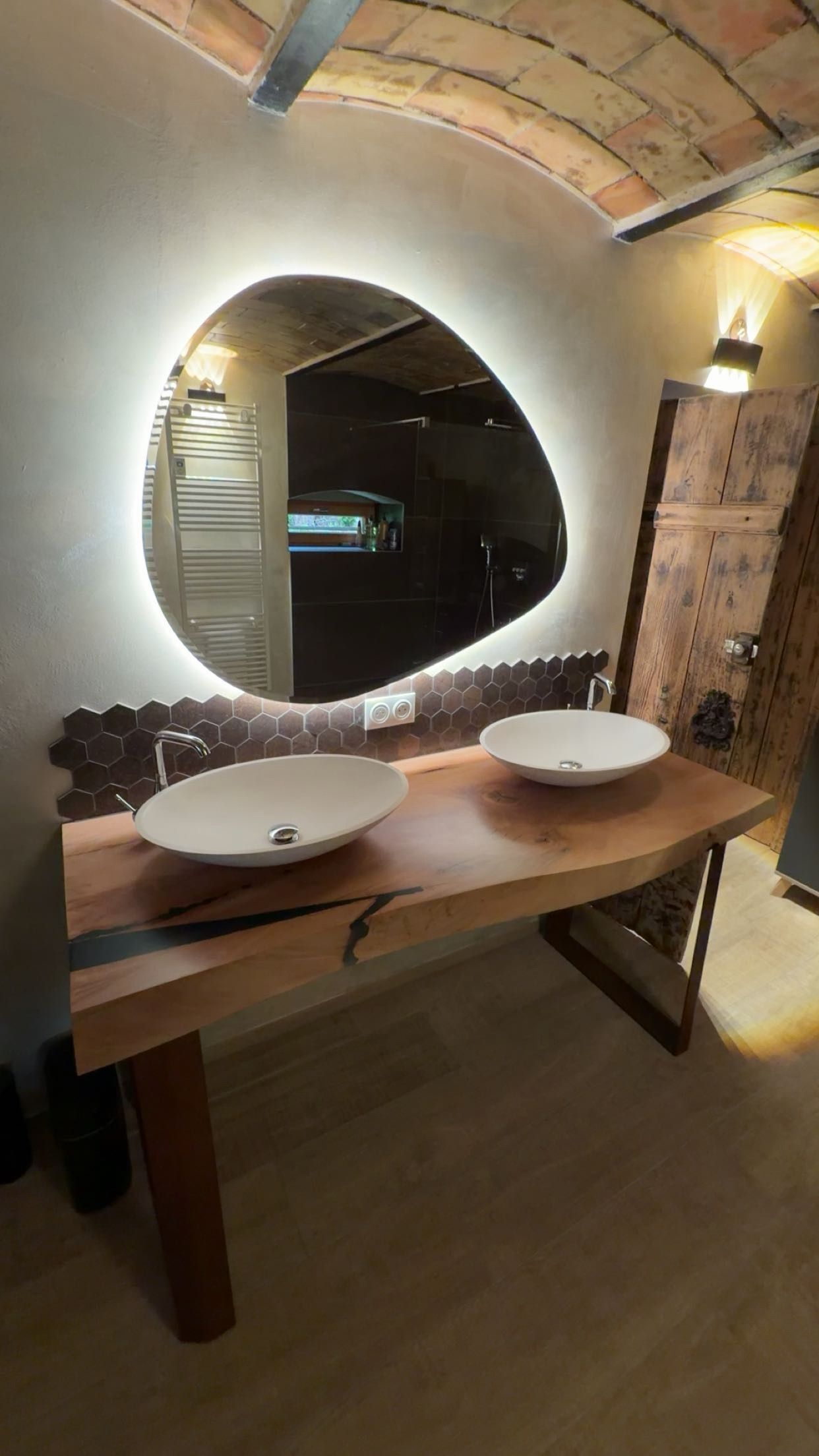 Salle de bains rustique avec meuble à double vasque, miroir ovale, plafond voûté en briques et éclairage chaleureux