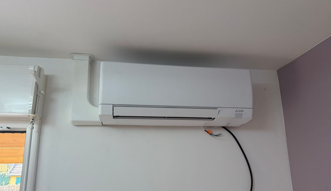 Climatiseur mural blanc avec un câble d’alimentation noir, dans l’angle d’une pièce.