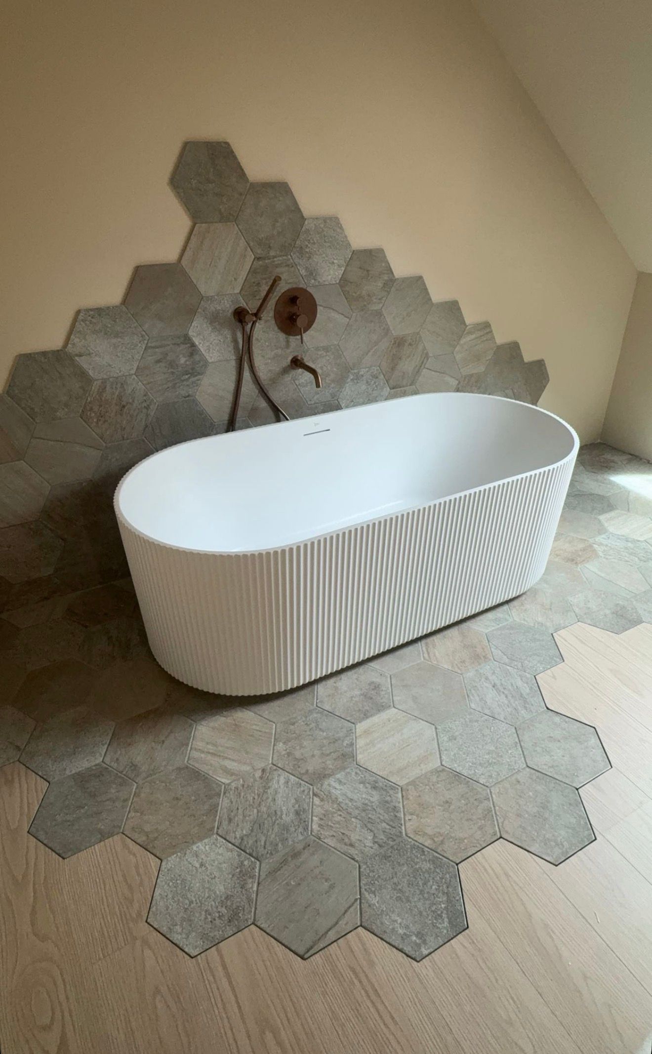 Baignoire blanche autoportante sur un sol en carrelage hexagonal dans une salle de bains moderne