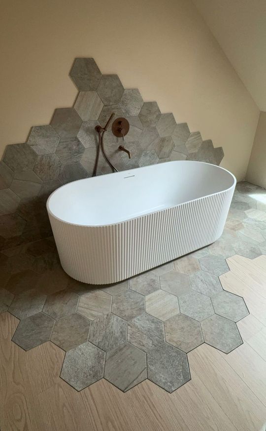 Baignoire ovale blanche sur un sol carrelé, dans un coin de salle de bains minimaliste
