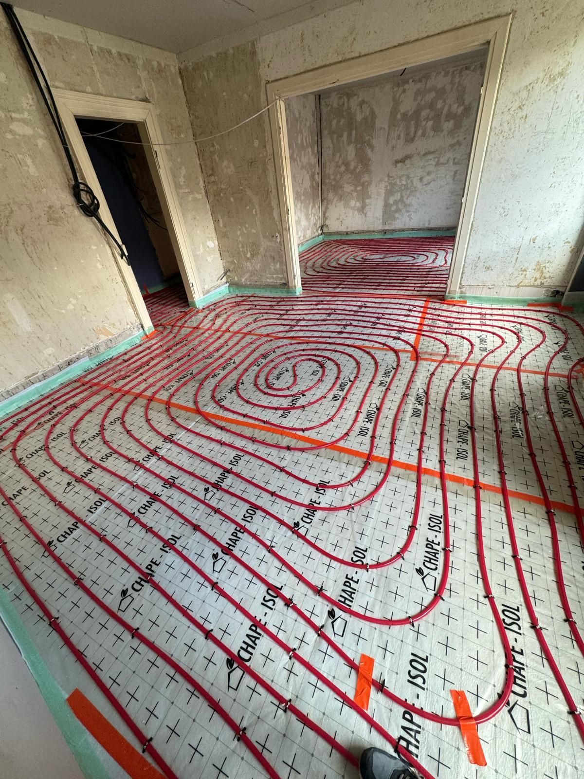Pièce intérieure en rénovation, avec des tuyaux rouges de chauffage au sol et des murs inachevés