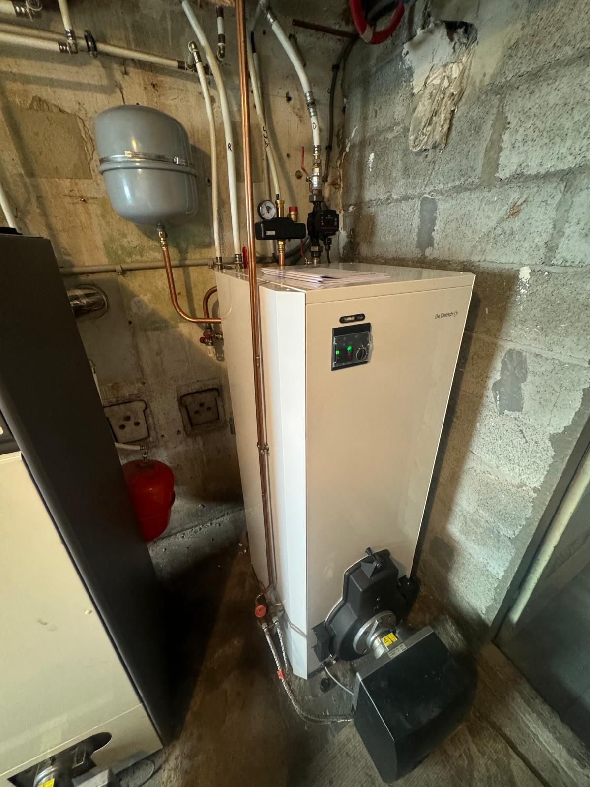 Buanderie avec une chaudière beige, des tuyaux et des équipements contre des murs en parpaings
