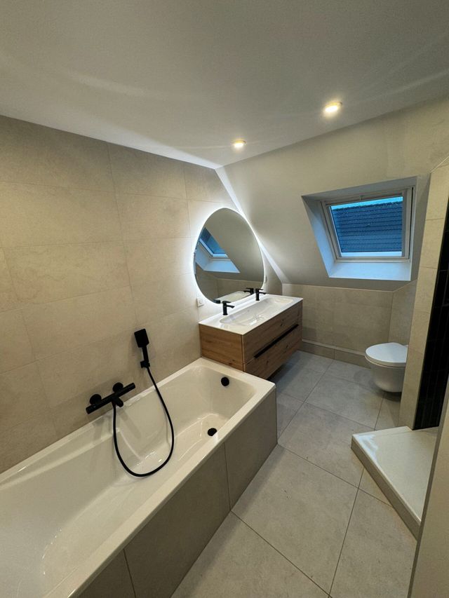 Salle de bains moderne avec baignoire, meuble vasque, miroir rond et fenêtre de toit
