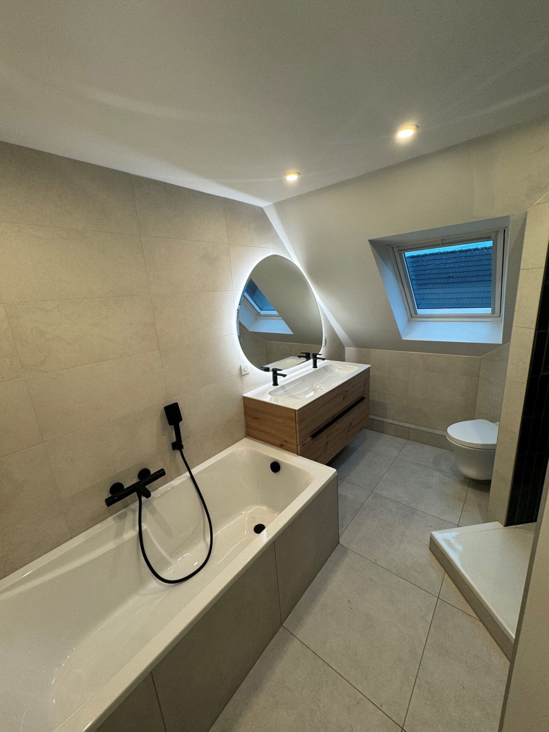 Salle de bains moderne avec baignoire, lavabo suspendu, miroir rond et fenêtre de toit