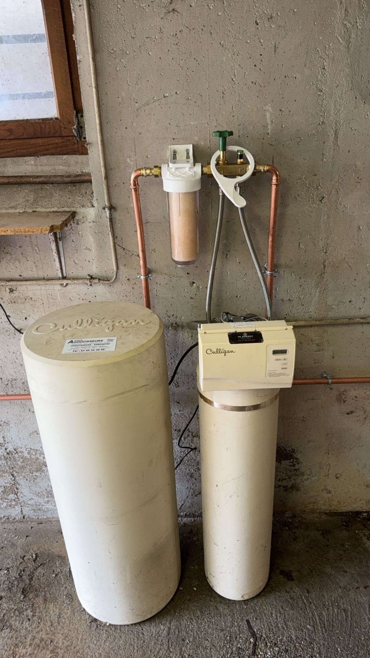 Deux cuves blanches de filtration de l’eau et un petit filtre avec des tuyaux fixés sur un mur en béton