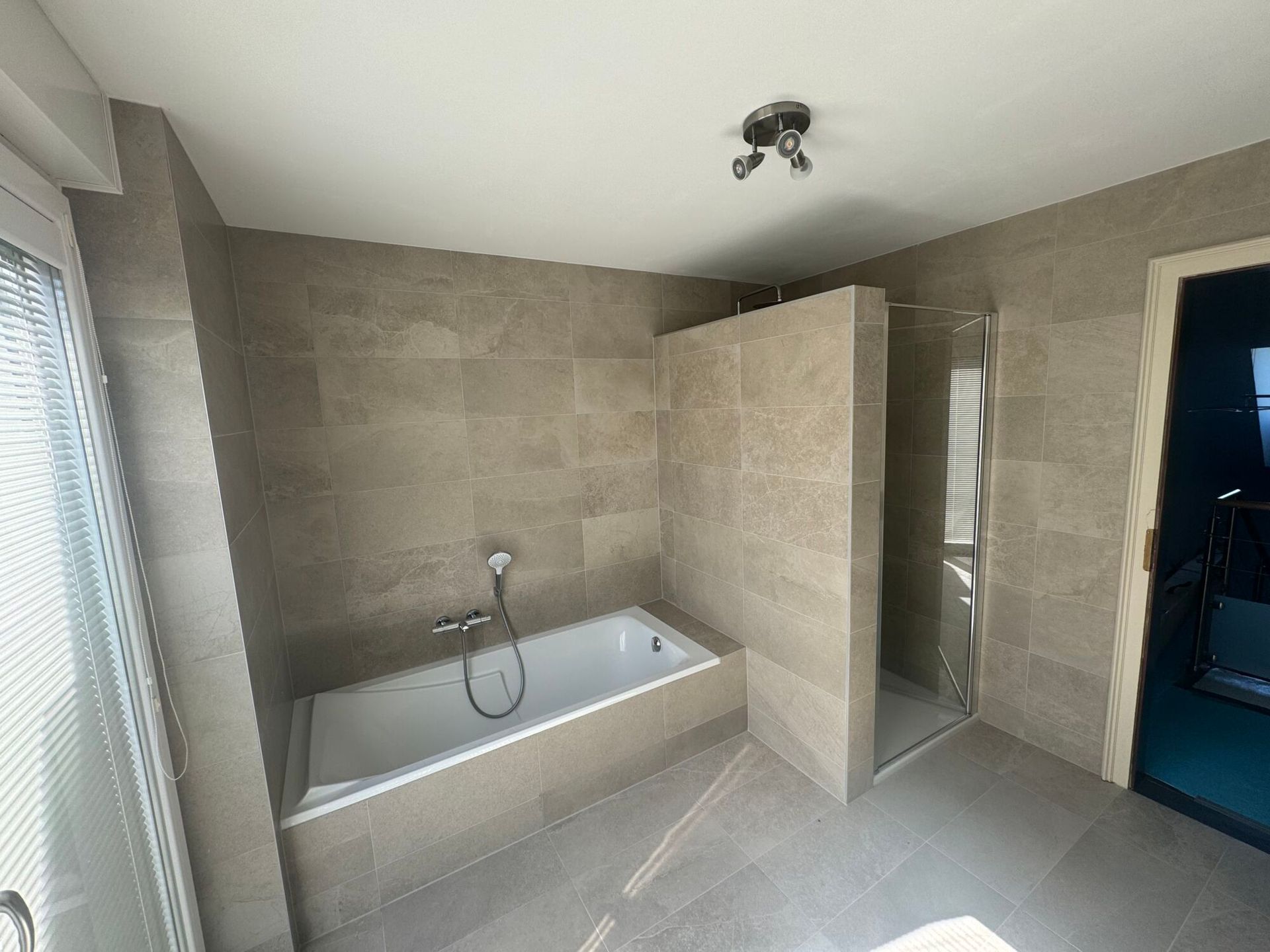 Salle de bains moderne carrelée de beige, avec une baignoire, une douche et une porte bleue
