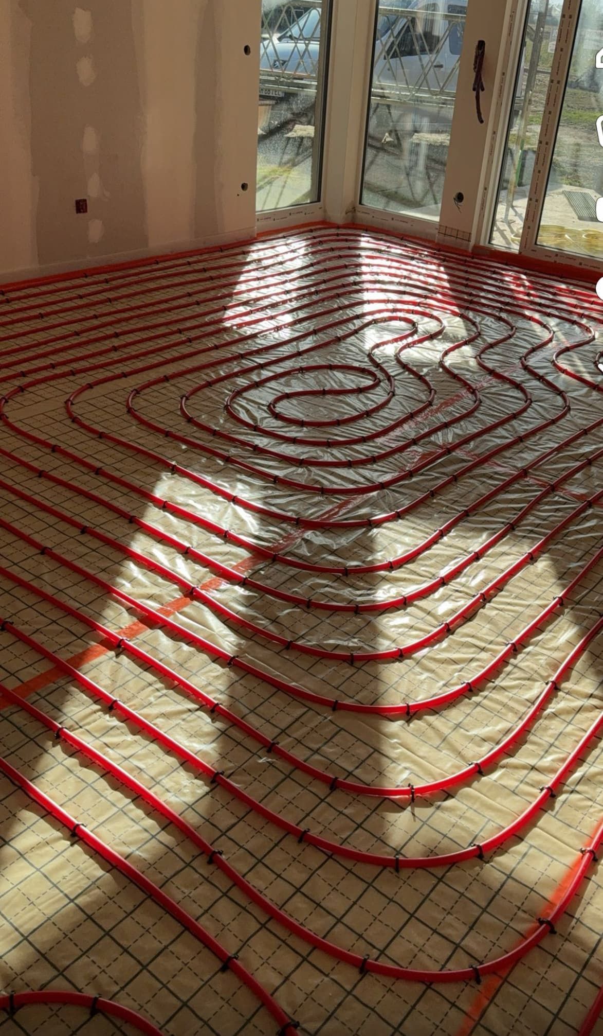 Des tuyaux rouges disposés en serpentin sur un sol en construction, près de hautes fenêtres.