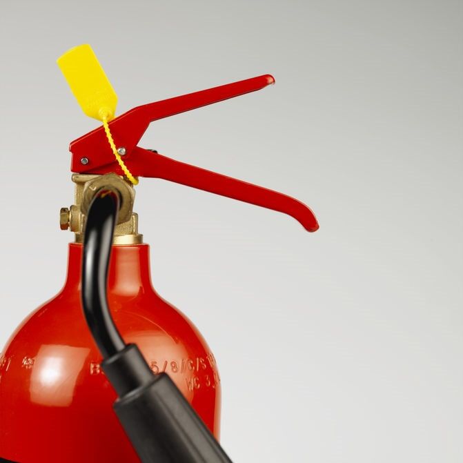 Extintor de incêndio vermelho, etiqueta de segurança amarela, mangueira preta, sobre um fundo cinza claro.