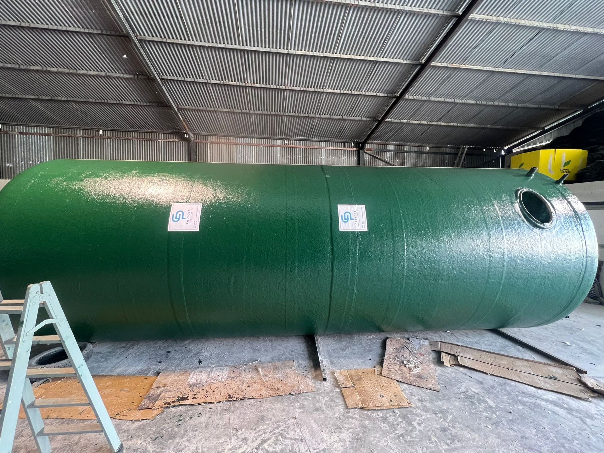 Un gran tanque verde está en un almacén al lado de una escalera.