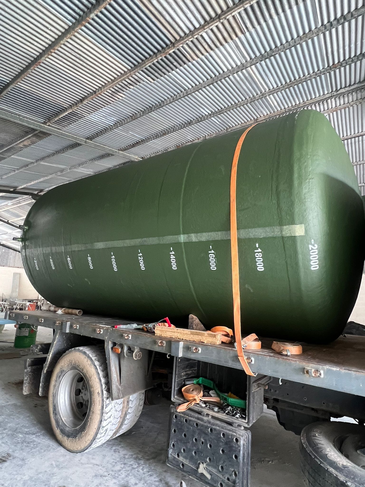 Un gran tanque verde está sentado encima de un remolque en un almacén.