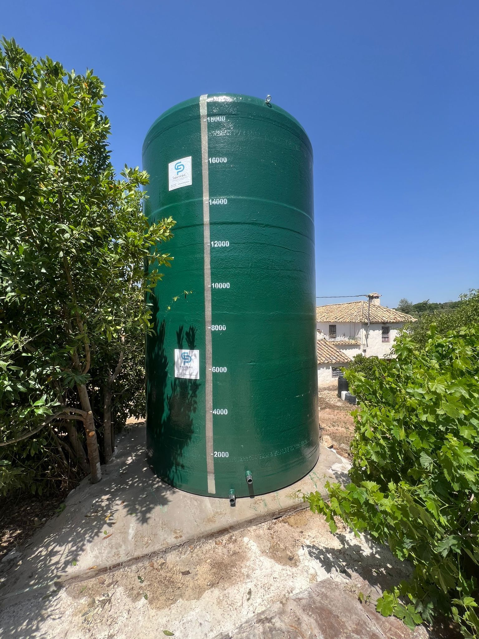 Un gran tanque verde está sentado en la cima de una colina de tierra rodeado de árboles.