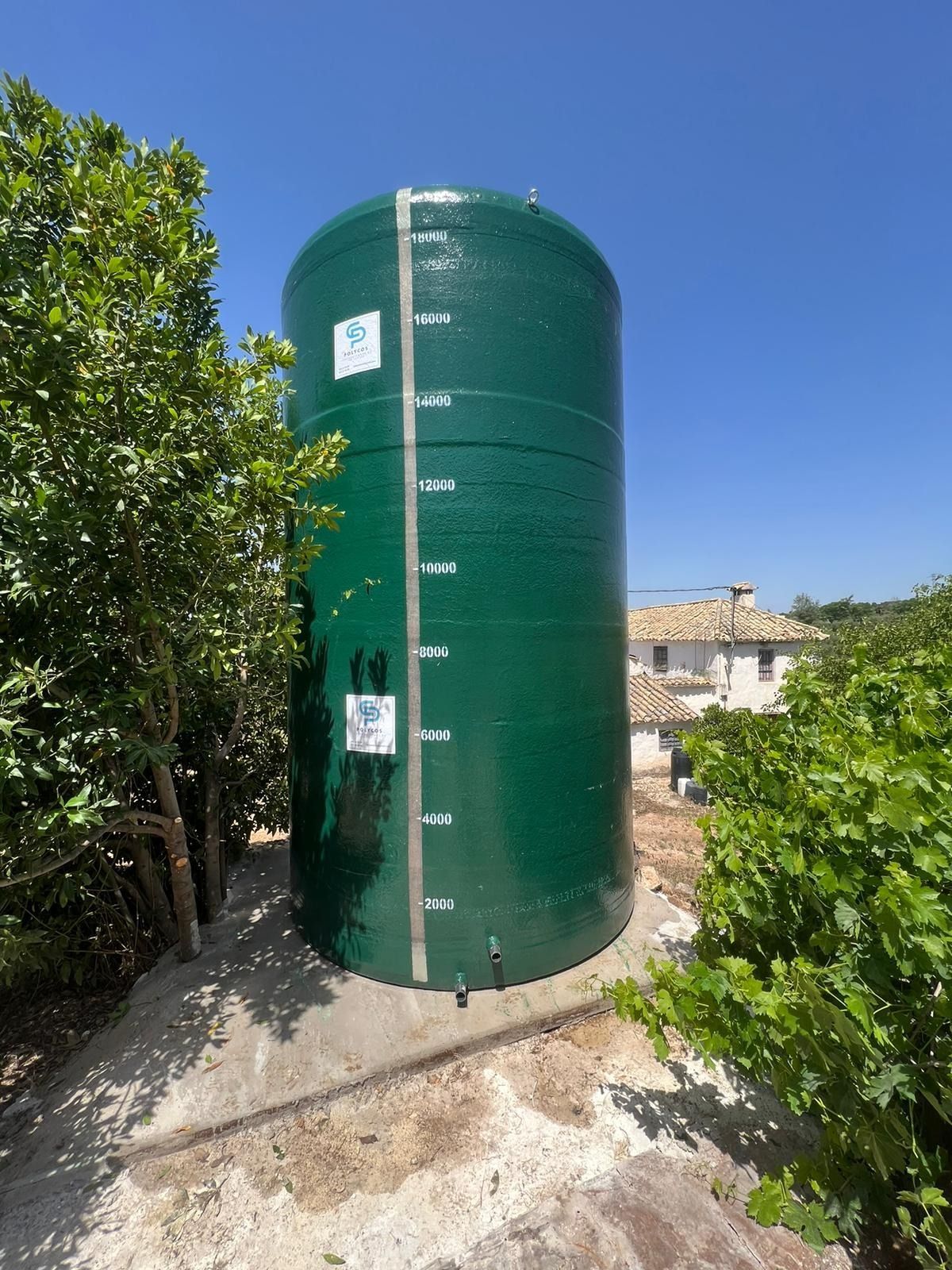 Un gran tanque de agua verde está rodeado de árboles y una casa.