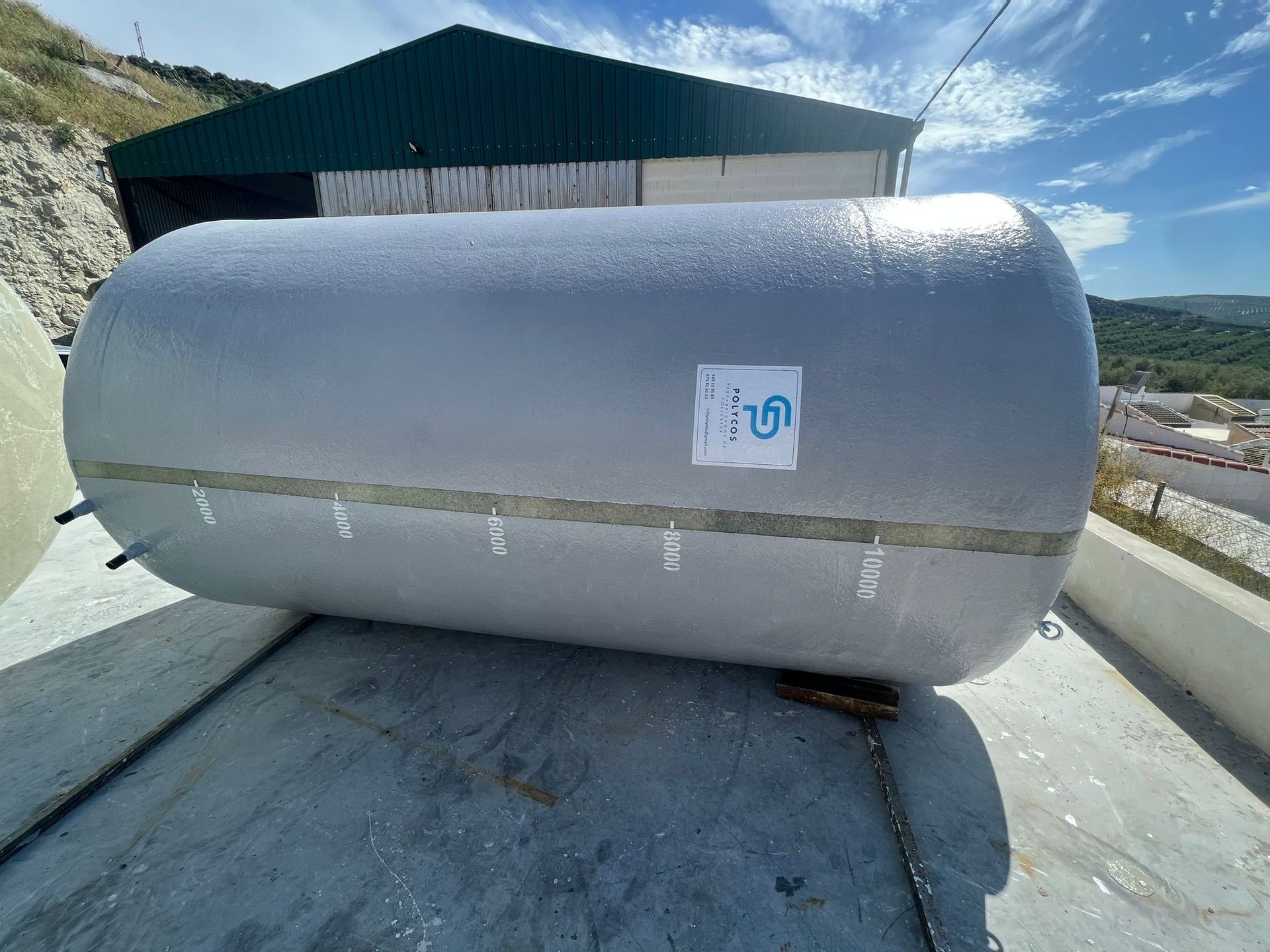 Un gran tanque gris está situado sobre una superficie de hormigón frente a un edificio.