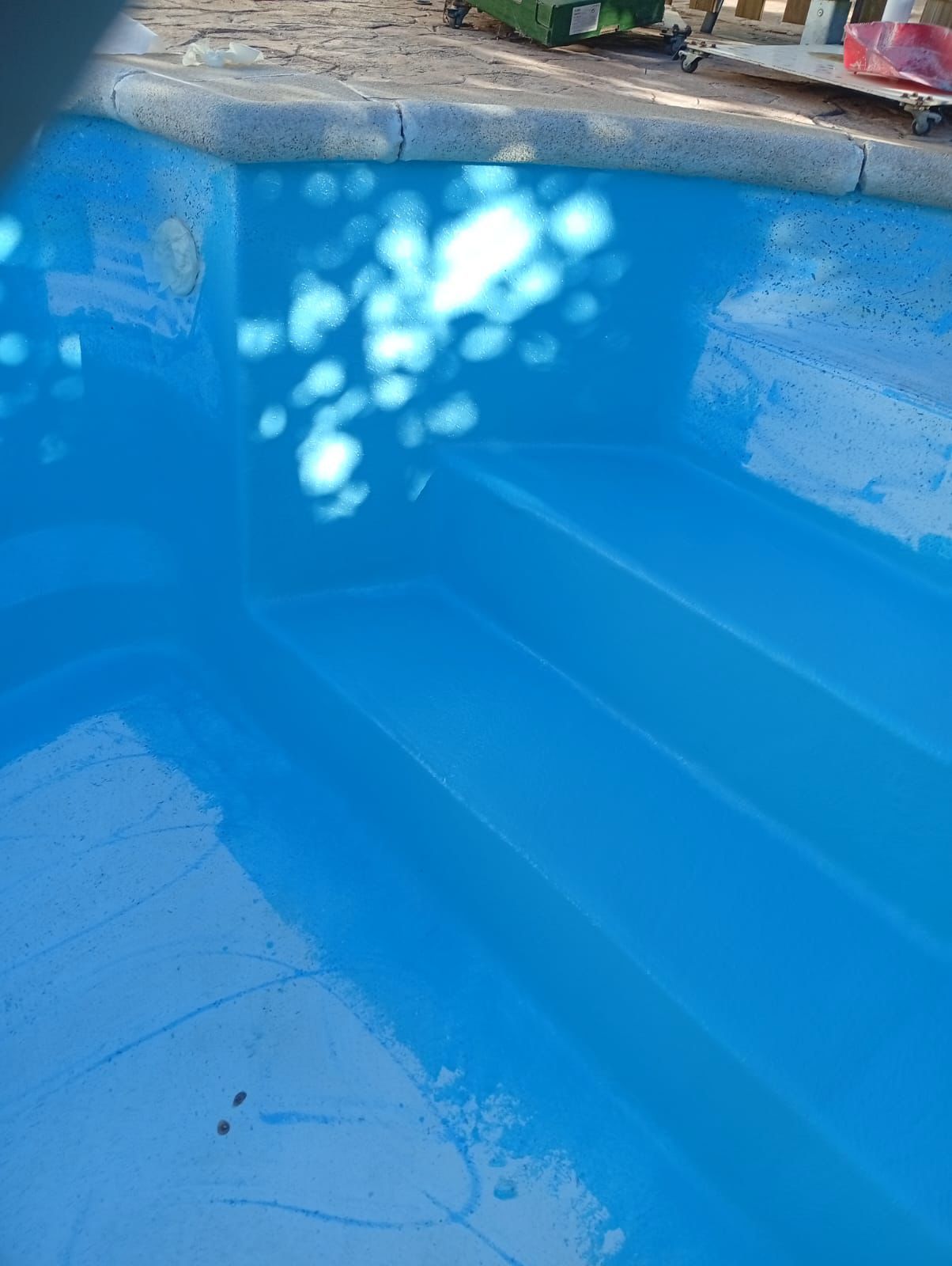 Piscina azul vacía con reflejos de la luz del sol en la superficie sin agua.
