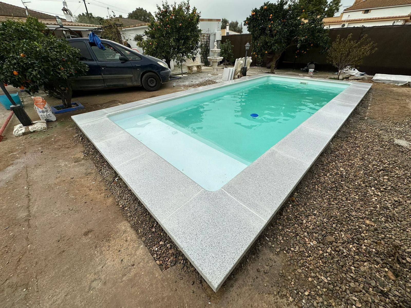 Piscina en el patio trasero con agua turquesa y una furgoneta oscura aparcada al lado.