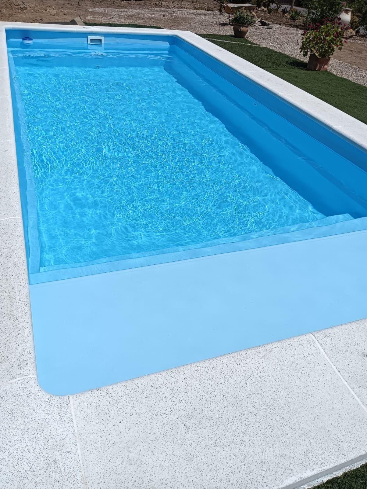 Piscina rectangular azul con terraza azul claro y borde de hormigón blanco al aire libre.