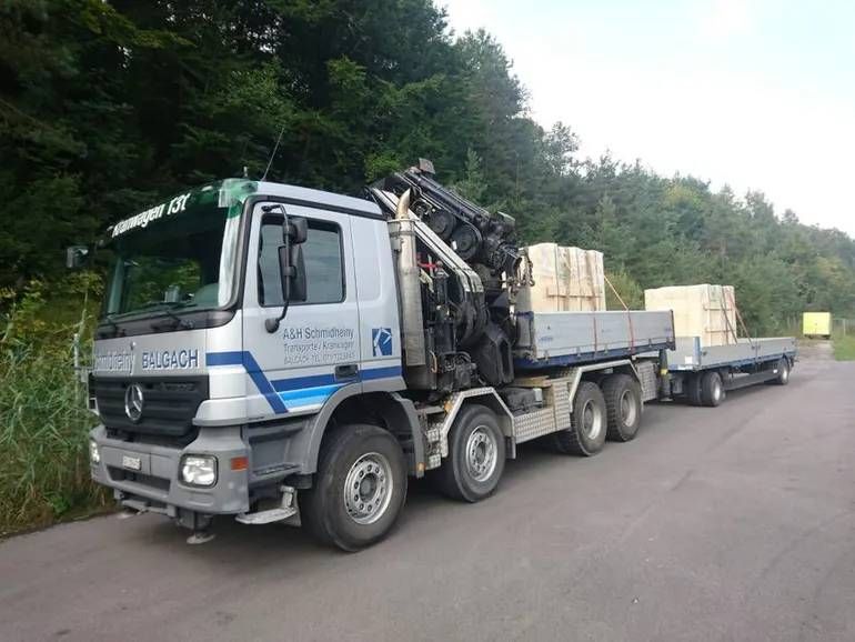 Ein weisser Pritschenwagen, beladen mit Kisten und Ausrüstung, parkte am Strassenrand neben Bäumen.
