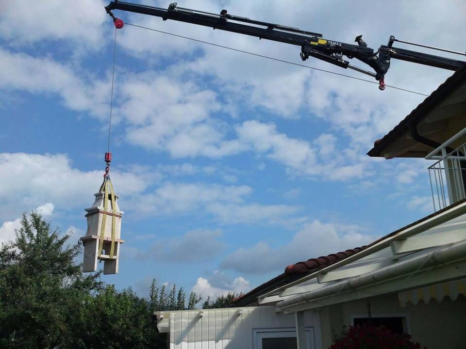 Ein Kran hebt einen kleinen Kirchturm unter einem bewölkten Himmel über die Dächer.