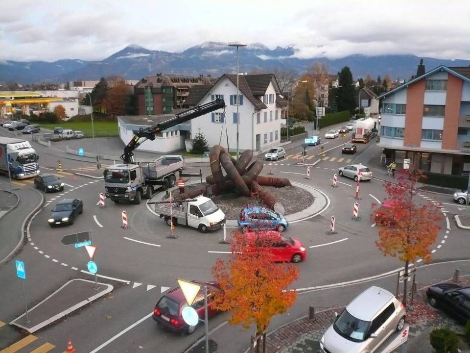 Kreisverkehr mit einer grossen Krabbenskulptur, Lastwagen und Autos in einer Stadtstrassenszene.
