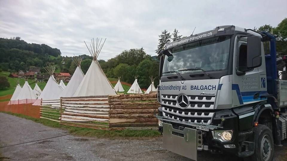 Weisse Tipis/Zelte neben einem blauen Lastwagen in einem bewaldeten Freigelände.