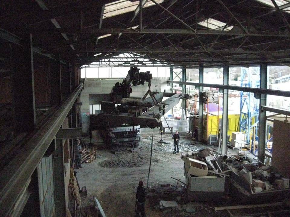 Beschädigtes Gebäudeinneres mit zerstörten Fahrzeugen, Trümmern und zerbrochenen Fenstern in einem grossen Industriegebiet