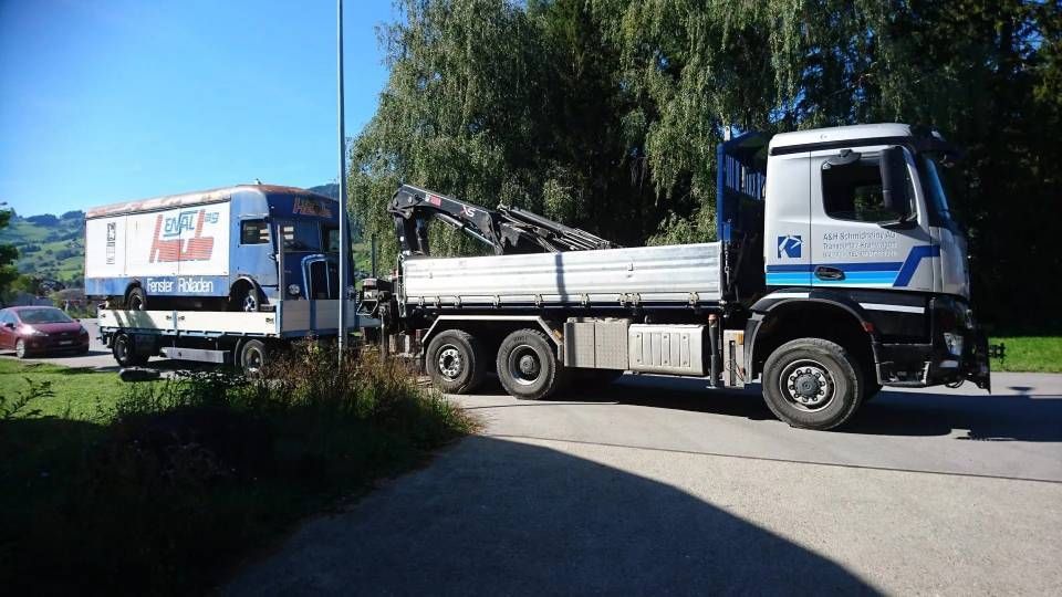 Zwei geparkte Lastwagen auf einer sonnigen Strasse, ein weisser Lastwagen vorne und ein blau-weisser dahinter.