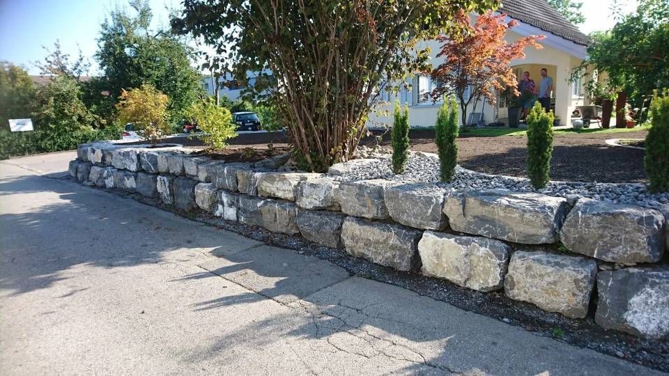 Eine Steinmauer säumt eine geschwungene Auffahrt neben einem gepflegten Vorstadthaus.